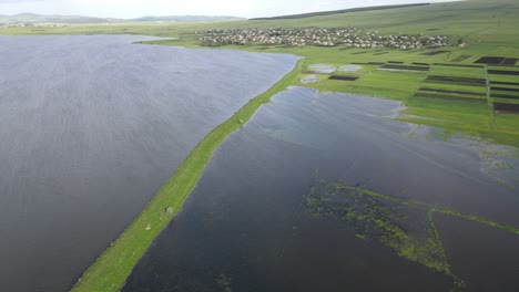 Aerial-shot-of-a-lake-surrounded-by-meadows-villages-old-houses-mountains