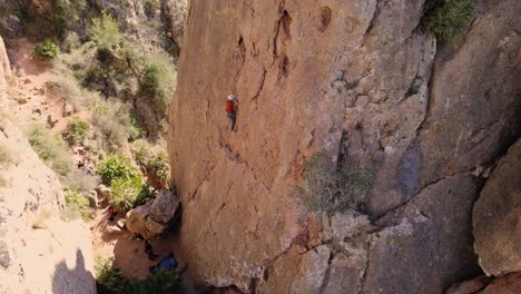 Man-rock-climbing-aerial-view-of-sportsman-rapelling-mountain-in-La-Panocha,-el-Valle-Murcia,-Spain-woman-rapel-down-a-mountain-climbing-a-big-rock