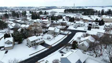 Aerial-view-of-a-suburban-neighborhood-blanketed-in-snow,-showcasing-houses,-trees,-and-streets-covered-in-a-layer-of-fresh-snow-in-the-USA