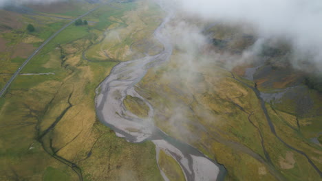 Misty-aerial-view-of-winding-river-through-lush-green-landscape-in-Glencoe,-Scotland