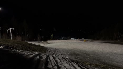 Vista-Nocturna-De-Una-Pista-De-Esquí-Con-Algunos-Parches-De-Nieve-Restantes-Iluminados-Por-Luces.