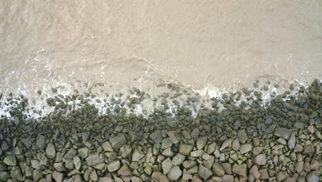 Sea-waves-hitting-rocks-on-a-sea-dyke,-overhead-drone-shot-descending