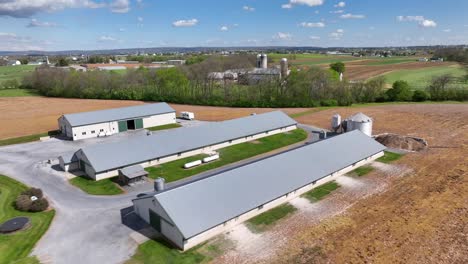 Aerial-view-of-a-sprawling-farm-in-Pennsylvania,-showcasing-large-agricultural-buildings,-green-fields,-and-surrounding-farmland-under-a-clear-blue-sky