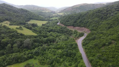 Aerial-view-of-mountains-village-country-road-in-beautiful-green-meadows-mountains-valley