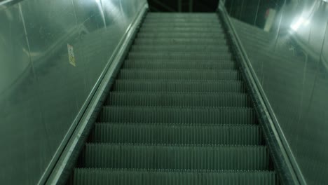 Escalera-Mecánica-Vacía-En-Una-Estación-De-Metro-Tranquila-Y-Poco-Iluminada,-Que-Transmite-Una-Sensación-De-Quietud-Y-Soledad-Urbana,-Superficies-Reflectantes