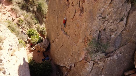 Man-rock-climbing-aerial-view-of-sportsman-rapelling-mountain-in-La-Panocha,-el-Valle-Murcia,-Spain-woman-rapel-down-a-mountain-climbing-a-big-rock