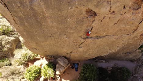 Man-rock-climbing-aerial-view-of-sportsman-rapelling-mountain-in-La-Panocha,-el-Valle-Murcia,-Spain-woman-rapel-down-a-mountain-climbing-a-big-rock