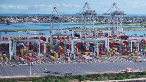 Revelación-Aérea-De-Camiones-Y-Grúas-Que-Manipulan-Contenedores-En-Webb-Dock-En-Port-Melbourne,-Australia