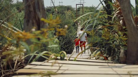 Plano-Completo-De-Padre-E-Hijo-Tomados-De-La-Mano-Mientras-Cruzan-Un-Puente-Colgante-Hecho-A-Mano