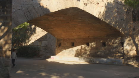 Shot-of-locals-walking-under-Puente-del-Mar,-a-pedestrian-bridge-that-crosses-the-river-Turia-in-the-city-of-Valencia,-Spain-on-a-sunny-day