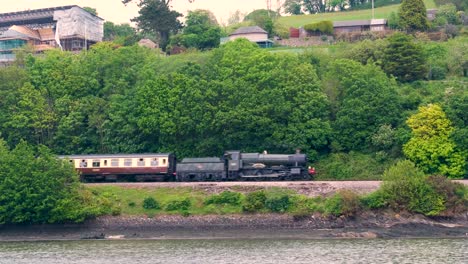 Historical-steam-train-traveling-alongside-River-Dart-from-Paignton-to-Kingswear-in-Dartmouth,-Devon-England-UK