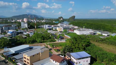 Dramatic-aerial-view-flight-of-krabi-town-in-southern-thailand,-showing-a-mix-of-buildings,-a-river,-the-sea,-and-forested-hills-in-the-background