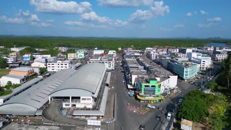 Magic-aerial-view-flight-of-krabi-town-market-hall-in-southern-thailand,-showing-a-mix-of-buildings,-a-river,-the-sea,-and-forested-hills-in-the-background