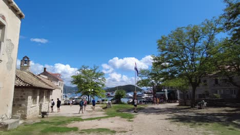 People-walking-in-a-sunny-village-square-near-the-waterfront-in-Elafiti-Islands,-Croatia