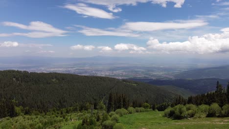 Drone-Volando-Sobre-La-Montaña-Vitosha,-Con-La-Ciudad-De-Sofía-En-La-Distancia-Y-Un-Hermoso-Cielo-Azul-Con-Nubes-Blancas-Arriba