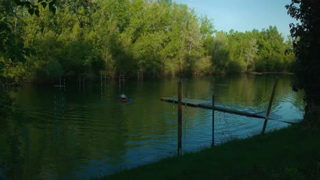 Person-kayaking-on-a-tranquil-section-of-Jarun-Lake-in-Zagreb,-Croatia,-surrounded-by-lush-greenery-and-a-small-dock