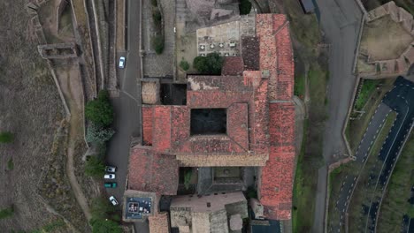 Cardona-castle-and-town-with-red-rooftops-and-surrounding-roads-and-greenery,-aerial-view