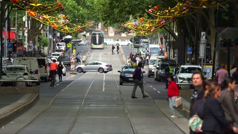 A-vibrant-Melbourne-street-scene-with-trams,-pedestrians,-vehicles,-and-festive-decorations-creating-a-bustling-urban-atmosphere,-slow-motion-shot