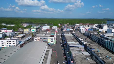 Best-aerial-view-flight-of-krabi-town-market-hall-in-southern-thailand,-showing-a-mix-of-buildings,-a-river,-the-sea,-and-forested-hills-in-the-background