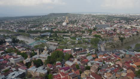 Aerial-shot-of-Tbilisi-Georgia-city-center-peace-bridge-Samiba-church-river-old-houses