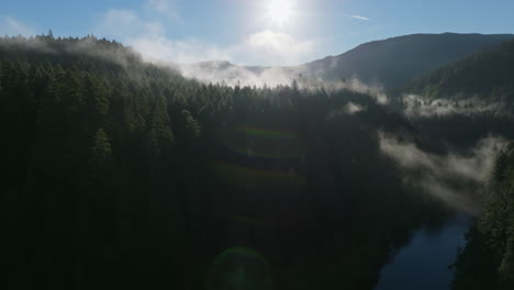 Panoramic-aerial-dolly-above-Lewis-River-Washington-to-the-sun-illuminating-fog-clouds