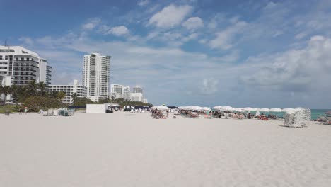 Sonniger-Tag-Am-Miami-Beach-Mit-Leuten,-Die-Unter-Sonnenschirmen-Faulenzen-Und-Einem-Klaren-Blauen-Himmel