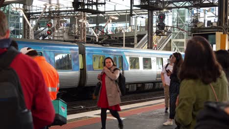 A-train-arrives-at-Southern-Cross-Station-in-Melbourne,-passengers-wait-on-the-platform-during-the-peak-hour-rush,-slow-motion-shot