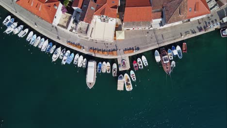 Moored-fishing-boats-aligned-along-marina-quayside-of-Milna-Town-harbor-in-Croatia,-Drone-top-down