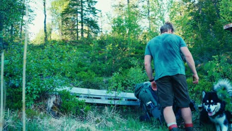 Excursionista-Mochilero-Con-Malamute-De-Alaska-Descansando-En-El-Banco-De-Madera-En-Medio-Del-Bosque