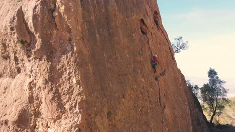 Man-rock-climbing-aerial-view-of-sportsman-rapelling-mountain-in-La-Panocha,-el-Valle-Murcia,-Spain-woman-rapel-down-a-mountain-climbing-a-big-rock