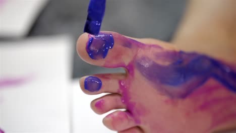 Detailed-closeup-of-paint-brush-spreading-purple-blue-paint-across-bottom-of-big-toe