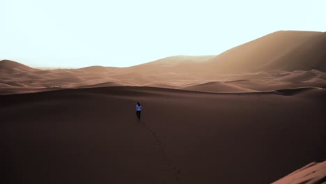 woman-walks-up-to-big-sand-dune-landscape,-epic-view-of-the-desert,-making-footsteps-in-sunny-dune