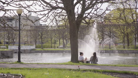 Two-female-friends-enjoy-picnic-next-to-lake-in-Kadriorg-Park,-Tallinn