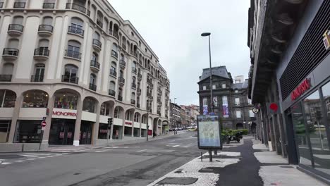 Straße-In-Clermont-Ferrand-Mit-Regierungsgebäude-Und-Nur-Ein-Paar-Autos-Und-Einem-Lieferboten-Auf-Einem-Fahrrad-Am-Wochenende