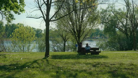 Gente-Sentada-En-Un-Banco-Bajo-Los-árboles-Junto-Al-Lago-Jarun-En-Zagreb,-Disfrutando-De-La-Tranquila-Vista-Del-Lago