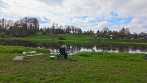 People-fishing-by-a-calm-river-at-Bauska-Fish-Festival-in-Latvia,-surrounded-by-green-landscape