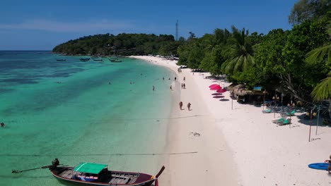 Touristen-Genießen-Einen-Sonnigen-Tag-An-Einem-Tropischen-Inselstrand-Mit-Traditionellen-Thailändischen-Longtail-Booten,-Die-Im-Türkisfarbenen-Wasser-Vertäut-Sind