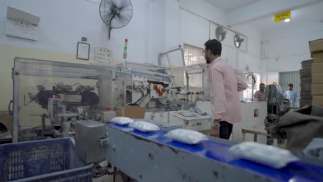 Verpackte-Seifenstücke-Bewegen-Sich-Entlang-Eines-Förderbands,-Während-Ein-Arbeiter-Die-Produktionslinie-In-Pakistan-überblickt