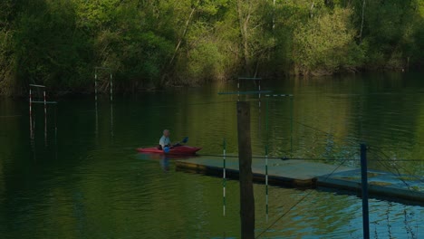 Persona-Navegando-En-Kayak-En-Un-Kayak-Rojo-En-El-Lago-Jarun-En-Zagreb,-Rodeado-De-Exuberantes-árboles-Verdes-Y-Una-Superficie-De-Agua-Tranquila