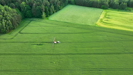 Vista-Aérea-De-Un-Tractor-Rociando-Un-Campo-Verde-Cerca-De-Una-Zona-Boscosa