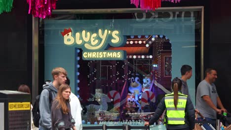 Slow-motion-shot-of-Bluey's-Christmas-display-on-Myer's-annual-Christmas-windows-in-bustling-downtown-Melbourne-City,-Bourke-Street-Mall,-with-pedestrians-passing-by