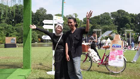 Happy-Smiling-Indonesian-Couple-Posing-For-Camera-With-Arms-Raised-At-Outdoor-Event-In-Park