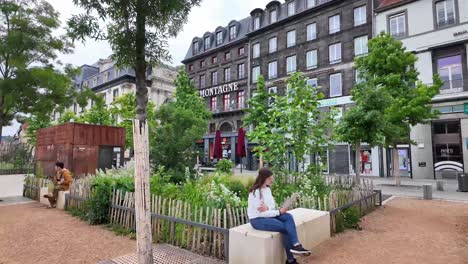 A-garden-on-the-public-square-in-the-middle-of-the-city-with-benches-and-people-reading,-resting,-Clermont-Ferrand,-France-on-weekend