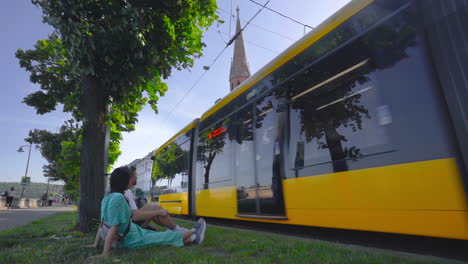 Reisendes-Paar-Sitzt-Auf-Dem-Rasen-Mit-Blick-Auf-Die-Reformierte-Kirche-In-Budapest,-Ungarn