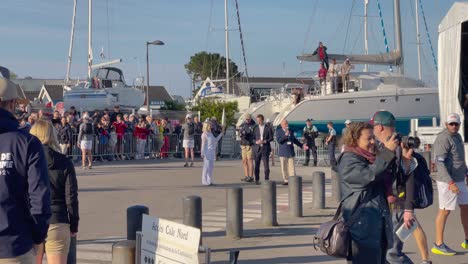 Blonde-lady-holding-and-showing-the-Paris-2024-Olympic-torch-flaming-on-a-sunny-day-in-France-surrounded-by-bodyguards-and-a-street-crowd