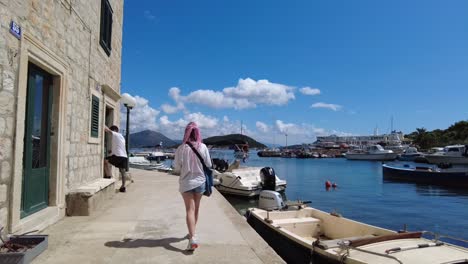 A-woman-walks-along-a-sunny-marina-in-the-Elafiti-Islands,-Croatia