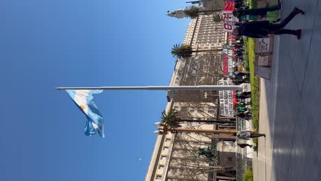 Argentinian-flag-waving-in-Buenos-Aires'-Plaza-de-Mayo-with-people-and-buildings-in-the-background