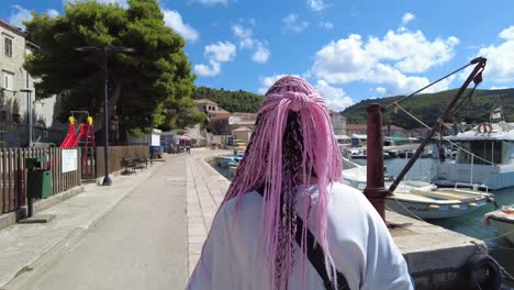 Woman-with-pink-braids-walks-along-a-harbor-on-a-sunny-day-in-Elafiti-Islands,-Croatia