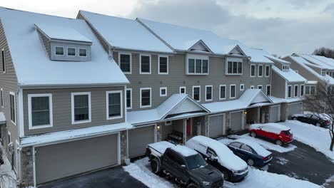 Aerial-view-of-snow-covered-townhouses-in-a-suburban-neighborhood,-showcasing-the-uniform-architecture-and-parked-cars-blanketed-in-snow