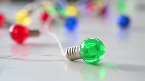 Seen-in-close-up-against-a-white-backdrop,-a-series-of-Christmas-LED-lights-brings-attention-to-a-sharply-focused-green-bulb,-amidst-a-background-of-blue,-red,-yellow,-and-green-bulbs